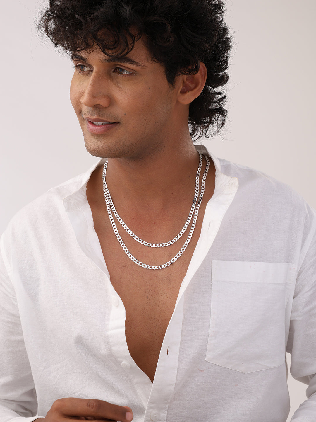 Man wearing a white shirt and multiple silver necklaces on a plain background